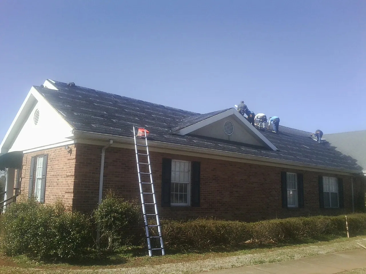 Crew tearing shingles off a brick ranch roof with a ladder set — Emergency Roof Repair work by our crew in Hathorne