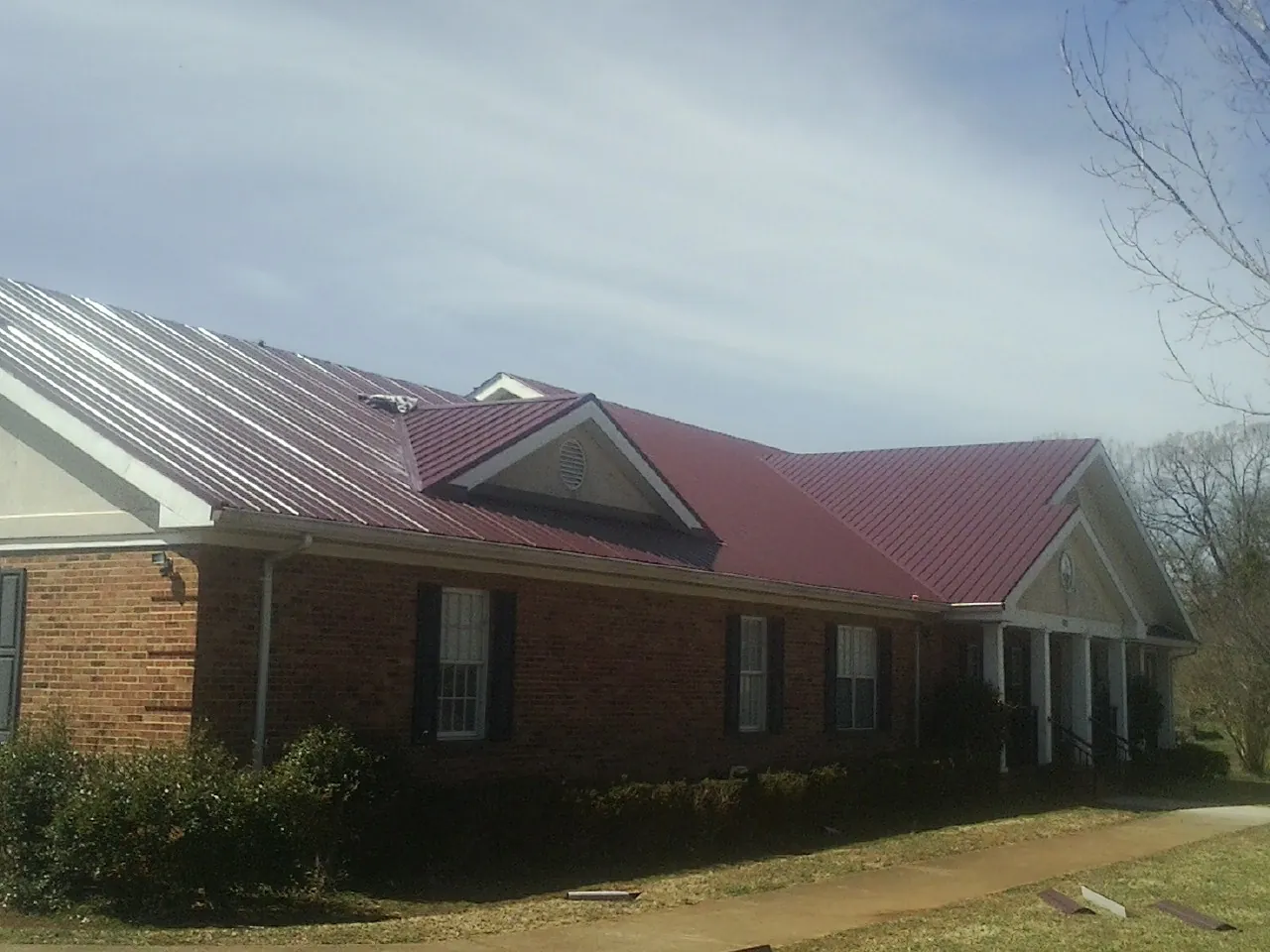 Red metal roof with gabled entries on a long brick building, from a Hail Damage Roof Repair job in Hathorne