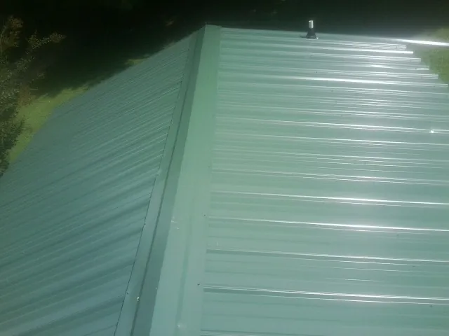 New green metal panels meeting at the ridge of a roof — Flat Roof Repair work by our crew in Hathorne