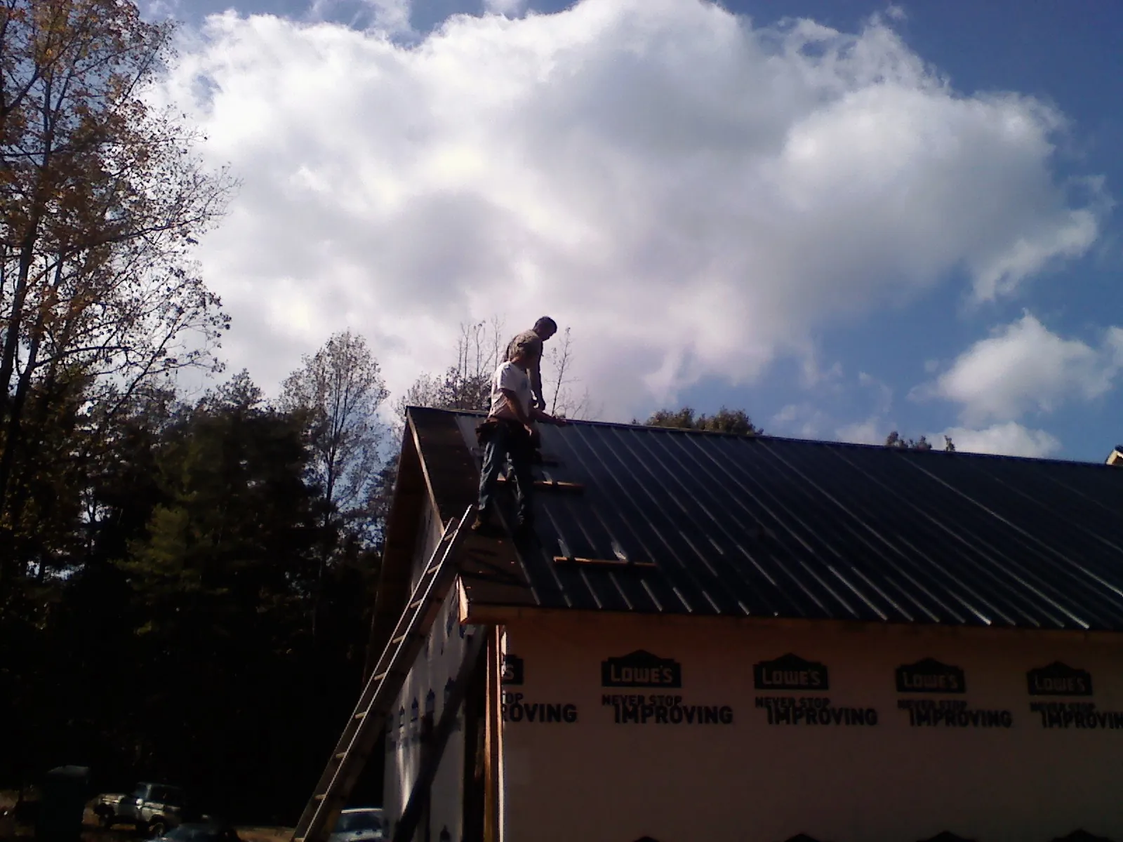 Roofer fastening dark metal panels high against a cloudy sky, from a Roof Inspection job in Hathorne