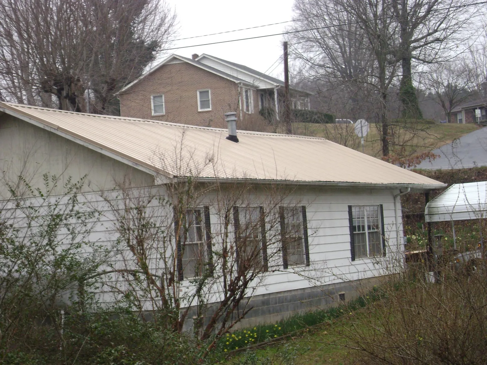 Tan metal roof on a white sided house set into a hillside — Commercial Roofing by Roofing Brothers in Hathorne