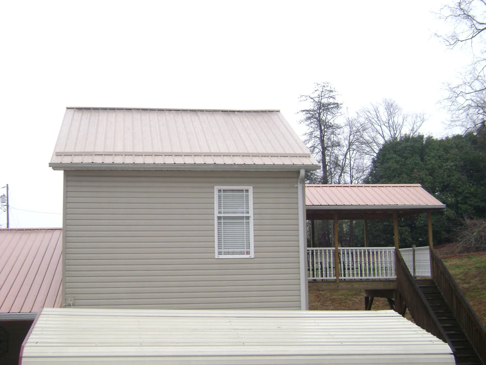 Tan metal roofs on a two story addition and attached porch, from a Roof Replacement job in Hathorne